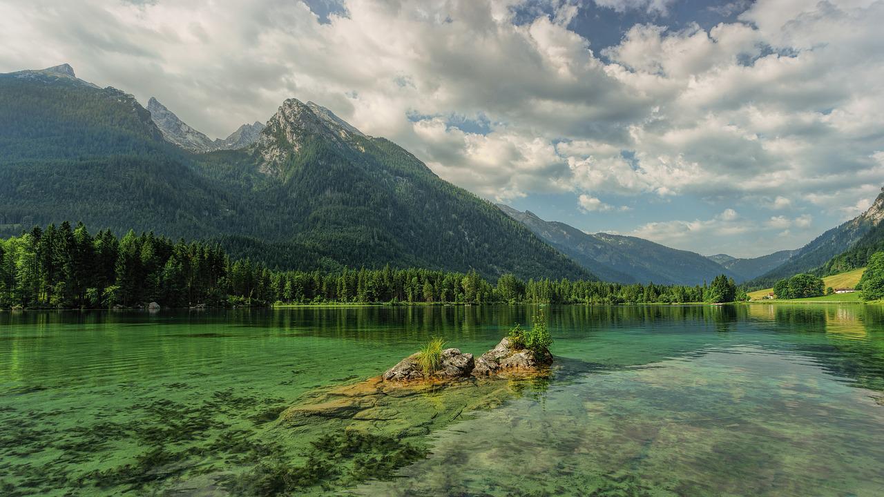 Klarer Bergsee mit bewaldeten Ufern und Berggipfeln unter Wolken