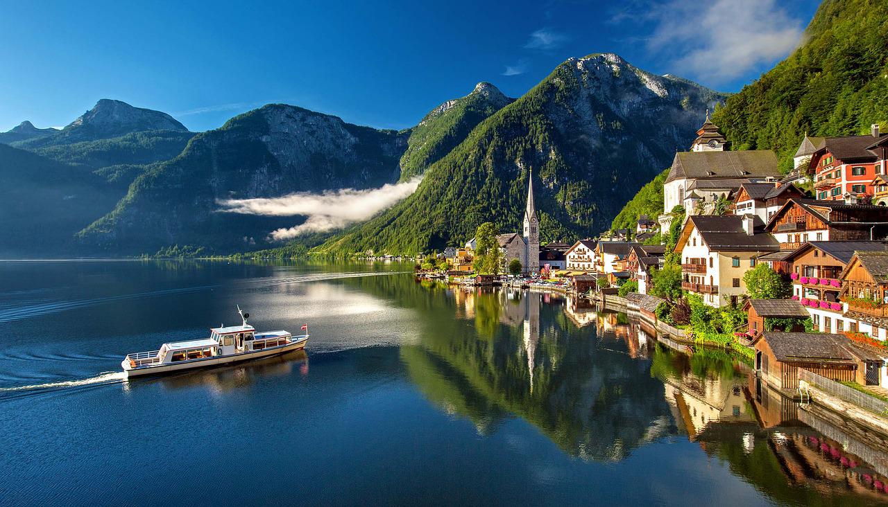 Ort mit Kirchturm am Ufer eines Bergsees, davor ein Ausflugsschiff