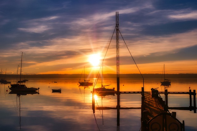 Segelboote und ein Steg an einem See bei Sonnenuntergang